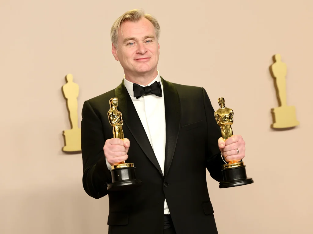 Cristopher Nolan che stringe in mano i suoi due nuovi premi Oscar: quello alla miglior regia e quello come miglior film entrambi ottenuti grazie ad Oppenheimer, grande successo del 2023