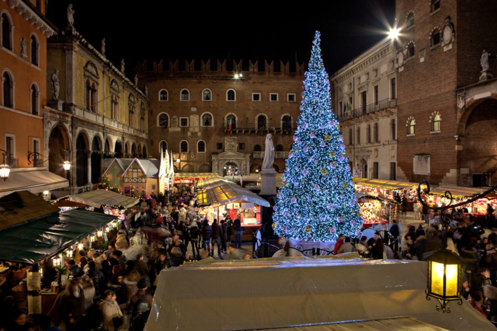 Albero di Natale Bauli in Piazza dei Signori di notte con, ai piedi, i passanti che esplorano i mercatini